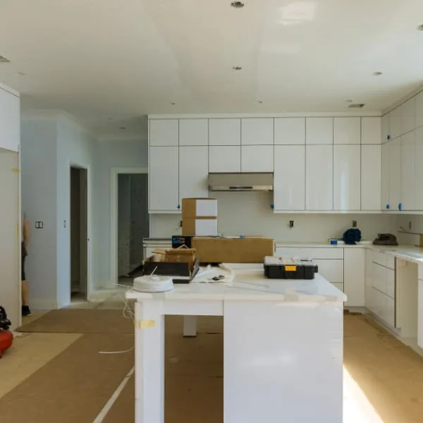 Cuisine moderne en rénovation avec armoires blanches, îlot central et outils de construction visibles.